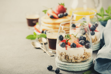 Healthy breakfast with oatmeal granola with berries and yogurt and panccakes on light gray concrete background. Healthy food concept with copy space. Retro style toned.