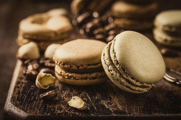 French coffee and pistachio macaroons with ganache filling with coffee beans on old wooden board on...