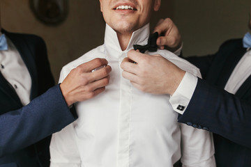 Groomsmen helping groom getting ready in the morning in the room. man hands putting on jacket and...