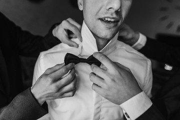 Groom getting ready in the morning with groomsmen in the room. man hands putting on jacket and bow...