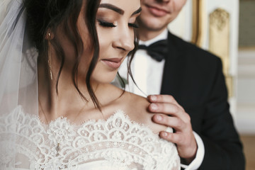 gorgeous bride with bouquet and stylish groom gently hugging in luxury room in hotel. rich wedding...