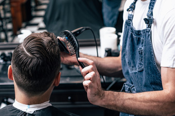 Naklejka premium The hands of young barber making haircut to attractive man in barbershop