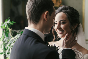 gorgeous bride smiling  and stylish groom gently hugging in luxury room in hotel. rich wedding couple embracing. romantic sensual moment of newlyweds in amazing classic indoors