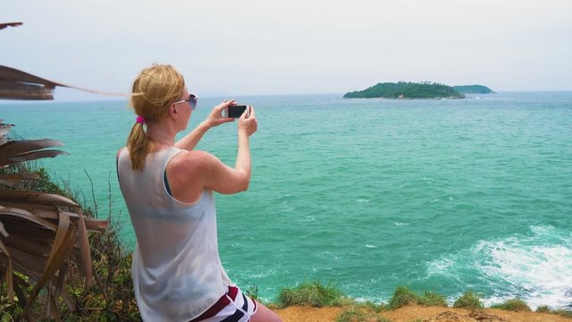 tourist girl takes pictures of a seascape with an island to the sea. Travel and tourism in the tropical islands.