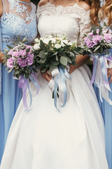 gorgeous bride and bridesmaids holding stylish bouquets. bride in white gown and bridesmaid in blue dress with purple bouquets posing outdoors at wedding reception
