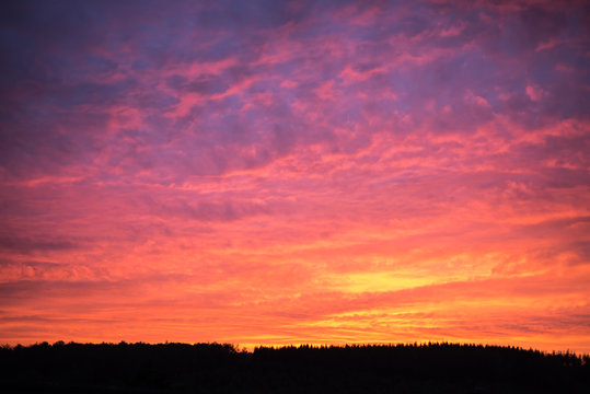 Fototapeta Scary red and orange sunset over a black mountain ridge.