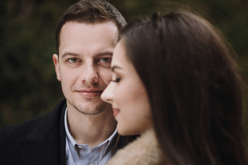 stylish groom looking and gorgeous bride embracing under  trees in winter forest. gorgeous wedding couple posing in winter snowy park. romantic sensual moment of newlyweds