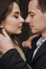 gorgeous bride in coat and stylish groom embracing under trees in winter forest. happy wedding couple gently hugging in winter snowy park. romantic sensual moment