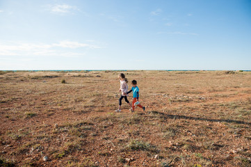two helpless refugees kids walking across desert with sea on horizon in hot summer day