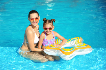 Young mother with little daughter in swimming pool on sunny day