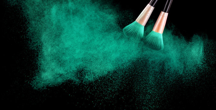 Cosmetics brush and explosion colorful makeup powder on black