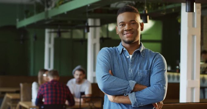 Portrait shot pf the cheerful African American youngman in the jeans shirt posing and smiling to the camera in the loft cafe.