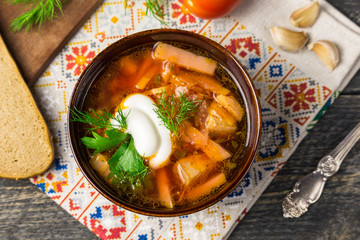 Borshch is a home-made Russian, Ukrainian and Polish national soup - red beetroot, vegetables and meat with sour cream on a gray wooden background with napkin, spoon, tomatoes, borscht with garlic