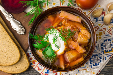 Borshch is a home-made Russian, Ukrainian and Polish national soup - red beetroot, vegetables and meat with sour cream on a gray wooden background with napkin, spoon, tomatoes, borscht with garlic