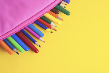 Colored Pencils school supplies in pink case yellow background. Back to School. Copy space for Text.