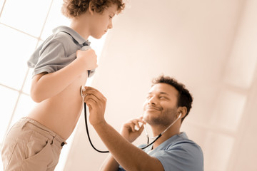 Deep in thoughts. Satisfied pediatrician keeping smile on his face and using stethoscope while examining heartbeats