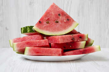 Many slices of watermelon on a round white plate, closeup. Side view.