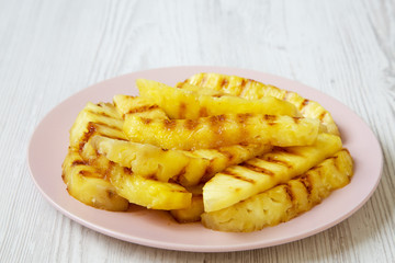 Grilled pineapple wedges on pink plate over white wooden background, side view. Summer food. Idea for snack. Closeup.