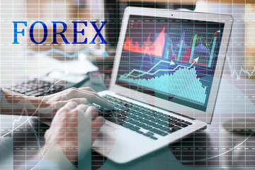 Double exposure of graphs and financial trader working with laptop at table in office. Forex concept