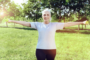 Strong woman. Cheerful positive elderly woman looking happy and proud of herself while exercising in a park