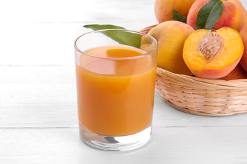 Ripe big peach in a basket and a glass of juice on a white wooden background close-up.