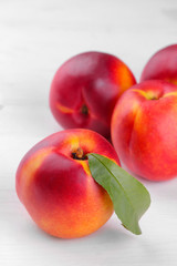 Ripe large nectarines with a green leaf close-up on a white wooden background