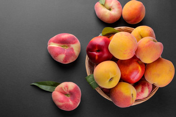 Many different varieties of peaches in a wicker basket on a black background. Top view