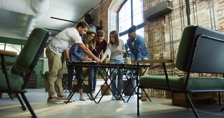 View from below on the mixed races group of startuppers standing at the table and planning the strategy of their business plan. Indoors.