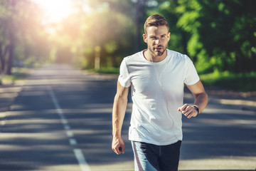 Waist up portrait of serious male running in park. He is listening to music with concentration while jogging. Copy space in left side