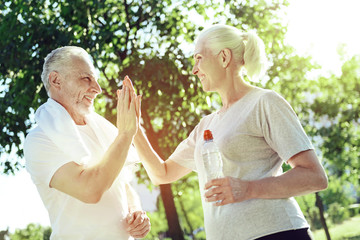 Congratulations. Positive active kind woman greeting her aged talented husband while being in a park with him