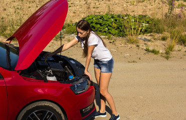 Fototapeta na wymiar A broken car on the road, the girl checks the oil level