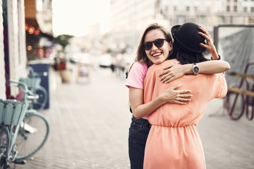 Positive girl hugging female friend. They standing on street during sunny day