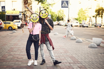 Full length portrait of cheerful man and smiling girl with emoji faces standing at street. Glad guy...