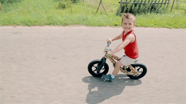 A little boy in a red t-shirt rides a running bike