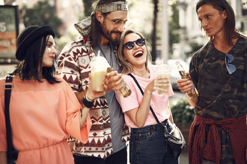 Laughing females and cheerful men drinking delicious liquid while going outdoor. They talking together