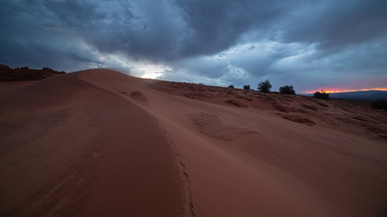 Fototapeta na wymiar Wind blows red sand over the curving line of a dune in Southern Utah