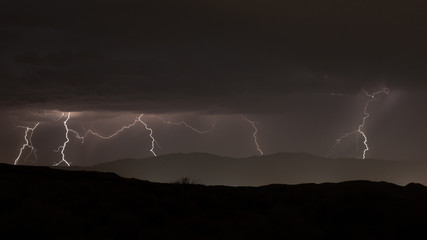 Naklejka na ściany i meble Lightning flickering over distant mountains at night