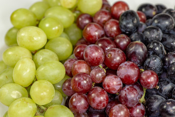 Black, red, green seedless grapes in a deep white bowl on a white tale waiting to be eaten