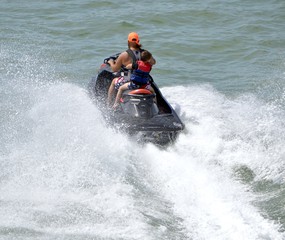 Fototapeta na wymiar Father and his young son riding tandem running waves on a jet ski.