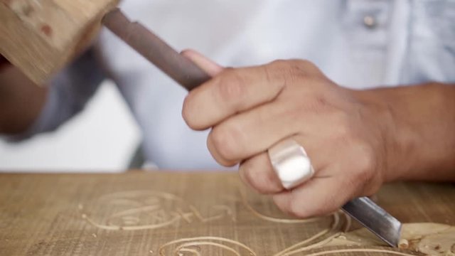 A SLOW MOTION MOVING CLOSE UP of a mallet hammering a chisel carving on a piece of wood