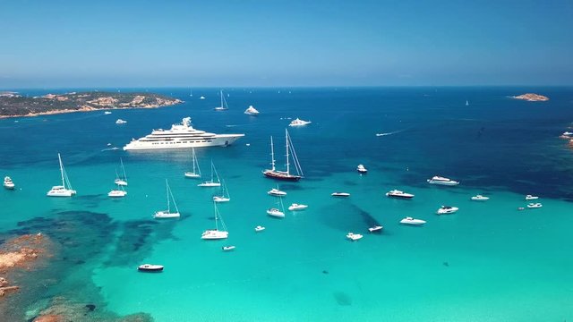 Aerial view of some yachts and a big luxury yacht on an emerald and transparent Mediterranean sea. Gulf of the Great Pevero, Emerard coast (Costa Smeralda), Sardinia, Italy.