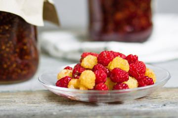 fresh raspberry on a plate and glass jars with raspberry jam on a wooden table, home-made preparations, cooking, homemade desserts
