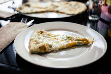 a piece of fresh hot pizza with cheese and Basil on a white round plate in the restaurant
