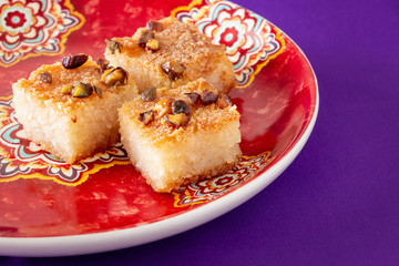 Three piecies Basbousa or Namoora - traditional arabic sweet semolina cake with nuts, coconut and orange blossom water. Copy space. Lilac background.