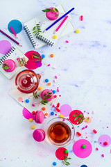 Glass teapot with candies and confetti on a light background with copy space. Pink and purple palette still life. Vibrant tea party drinks flat lay.