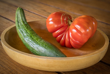 Big red heart-shaped tomato and cucumber in a wooden bowl
