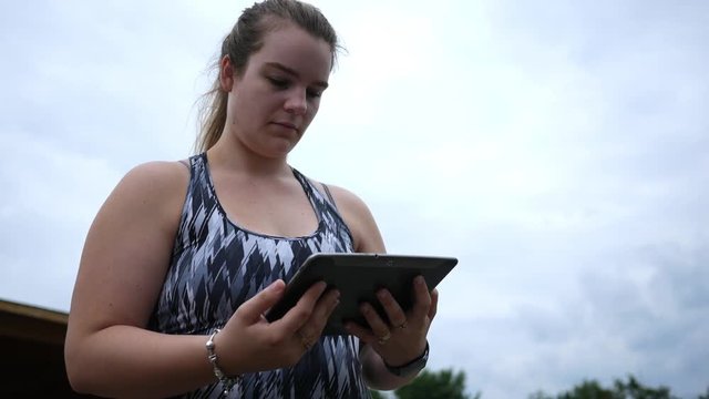 Camera pans to blonde woman in jogger clothes reading a tablet screen