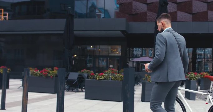 TRACKING Handsome young adult man wearing suit having a coffee before riding his classic bicycle to work in the morning. 4K UHD 60 FPS SLOW MOTION
