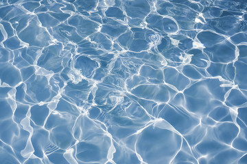 Blue water surface with bright sun light reflections, water in swimming pool background closeup