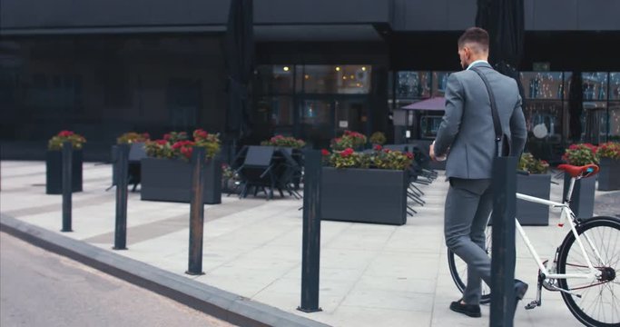 TRACKING Handsome young adult man wearing suit having a coffee before riding his classic bicycle to work in the morning. 4K UHD 60 FPS SLOW MOTION